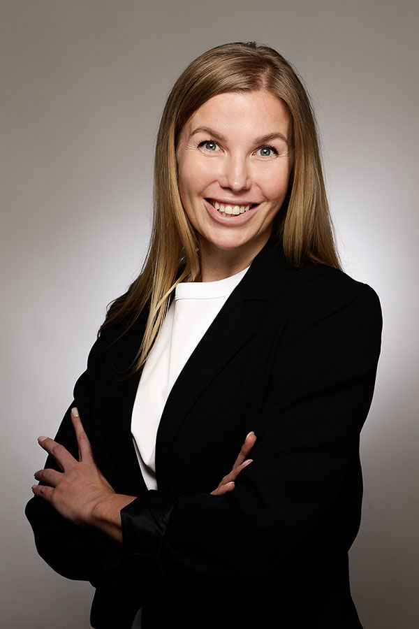 Geschäftsfrau mit langen blonden Haaren im schwarzen Blazer vor neutralem Hintergrund<br />
